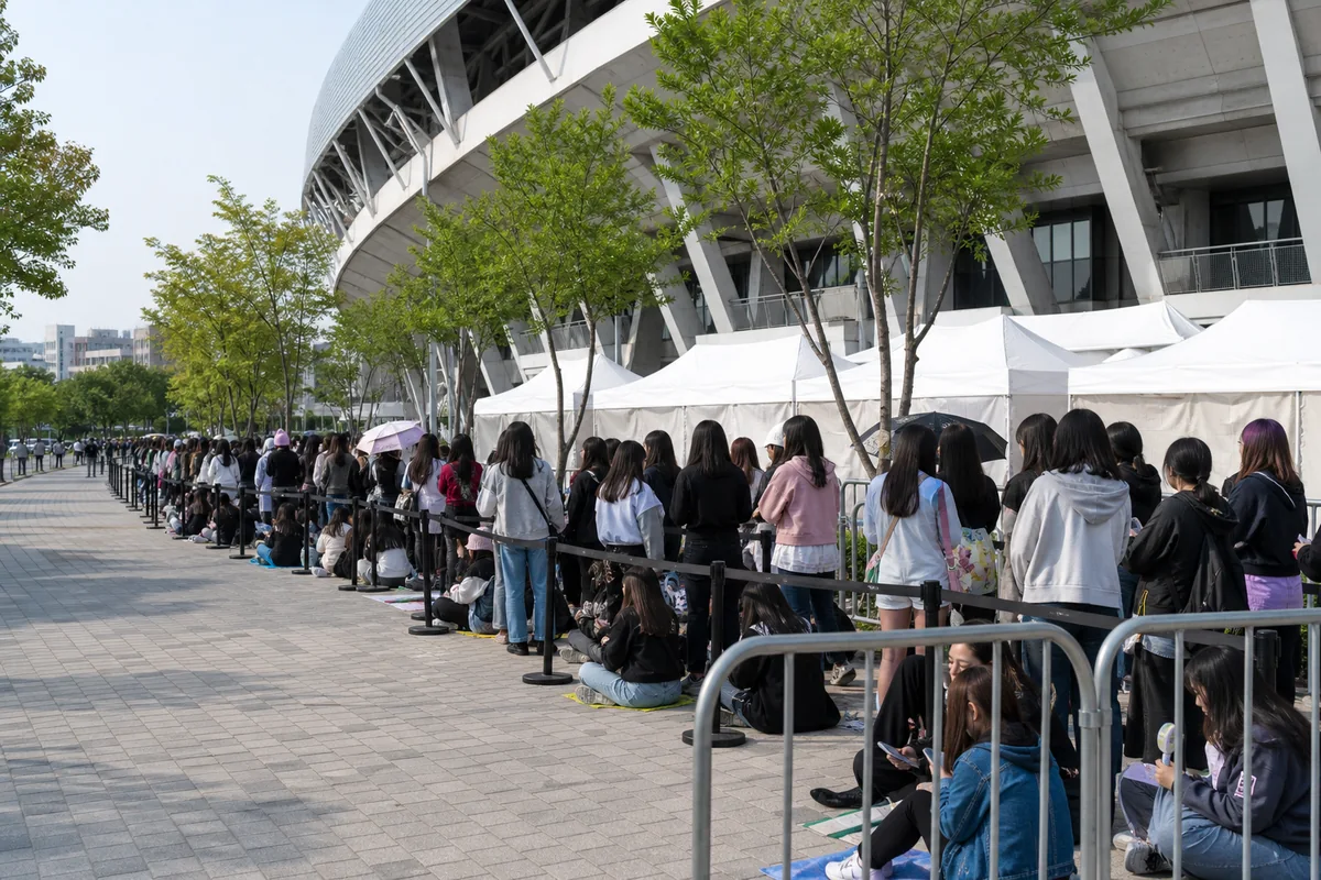 k pop concert merch booth queue with numbered tickets and organized fan line